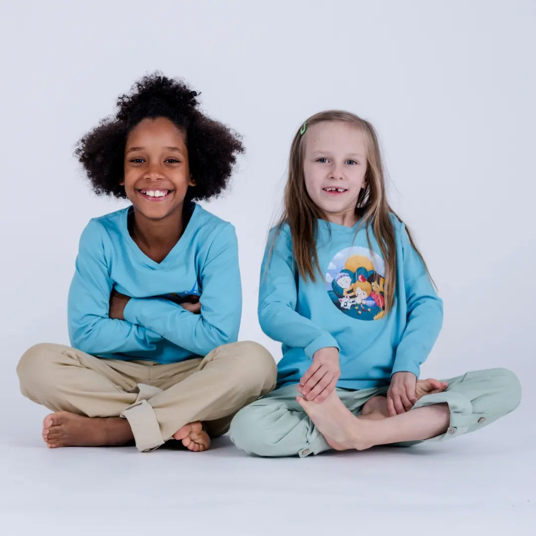 Zwei Kinder sitzen im Schneidersitz mit aqua blauen Unisex Larmshirts