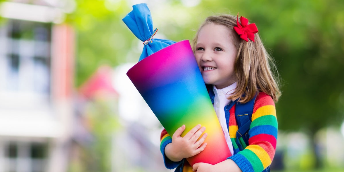 Kind mit Regenbogen-bunter Schultüte und Weste, lächelnd am Tag der Einschulung