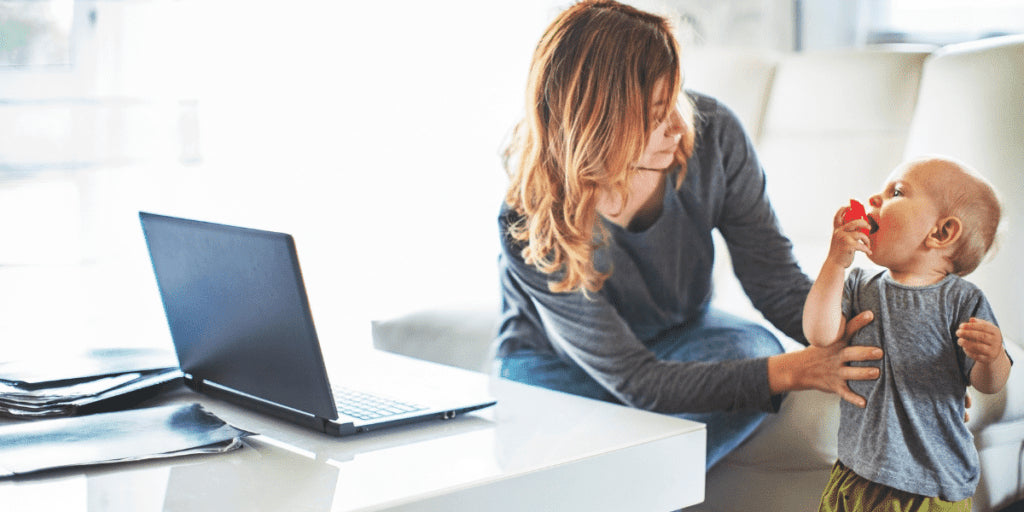 Working Mom vor Laptop beugt sich zum Kleinkind