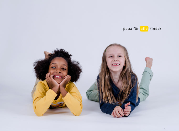 Zwei Kinder liegend und lachend mit pauakids Unisex Kinderkleidung