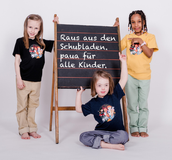 3 diverse Kinder vor Schulspieltafel, mit Text: Raus aus den Schubladen. paua für alle Kinder