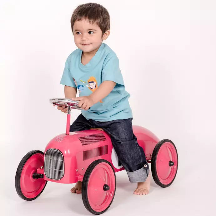 Kind auf Vintage Rutschauto mit pauakids Hose und Shirt, das lächelt verschmitzt