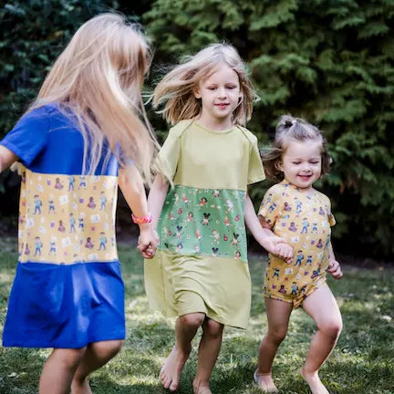 Drei Kinder, zwei mit pauakids Kleidern, eines mit pauakids Wickelbody, laufen im Garten
